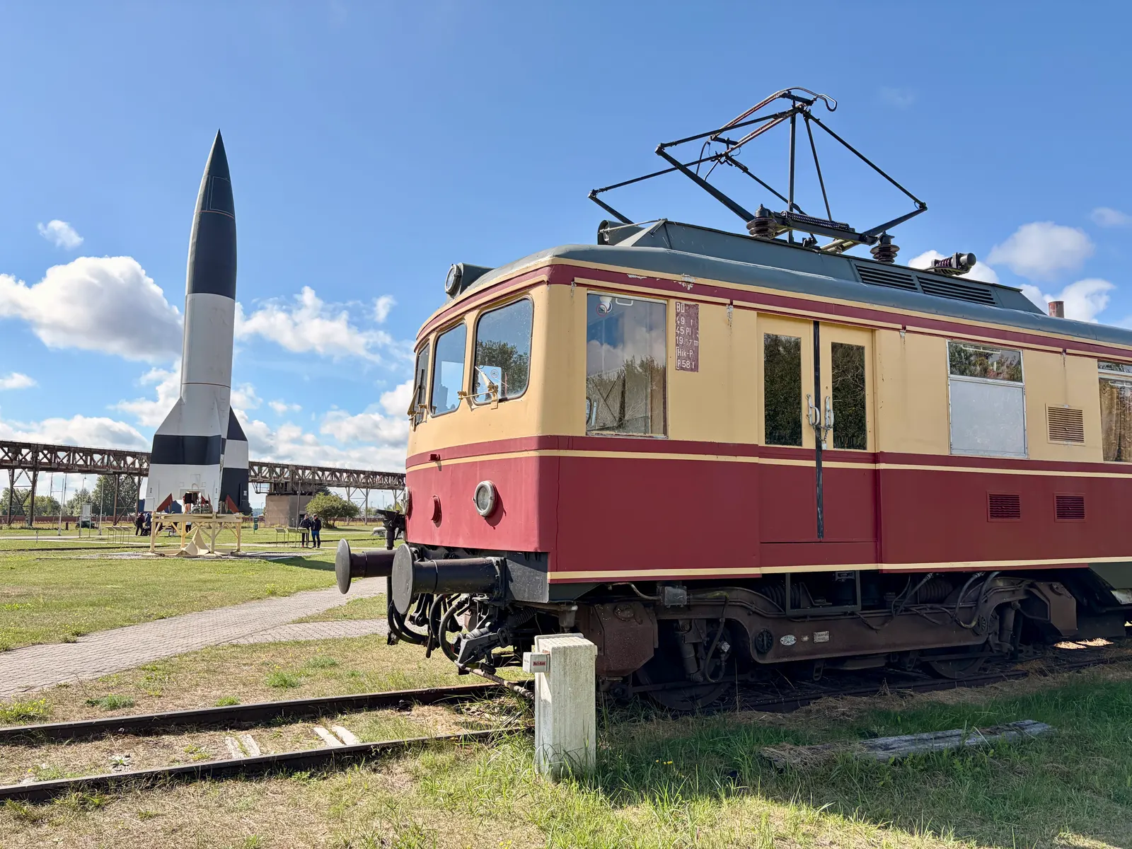 Historische rot-beige Elektrolokomotive auf Museumsgleis, dahinter eine V2-Rakete auf dem Gelände des Historisch-Technischen Museums Peenemünde.