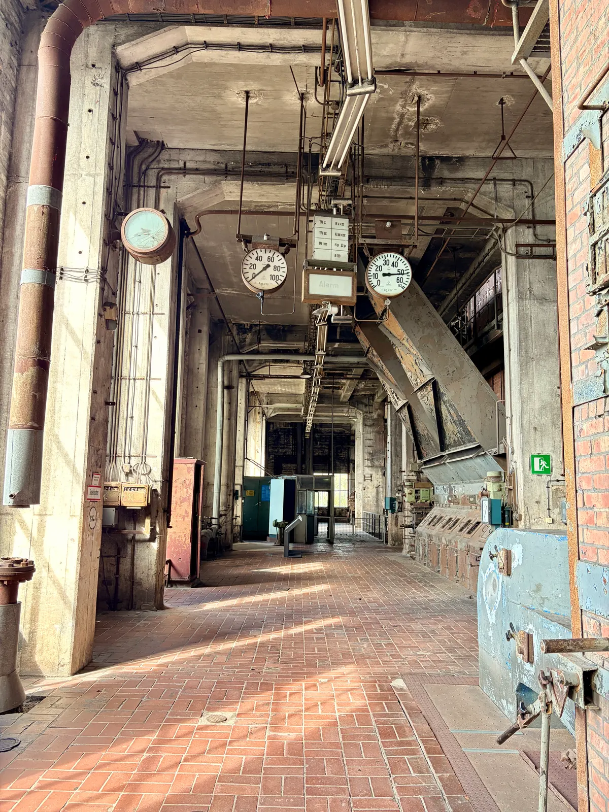 Industrieflur im ehemaligen Kraftwerk mit Rohrleitungen, Messuhren, Backsteinboden und alter Förderanlage.