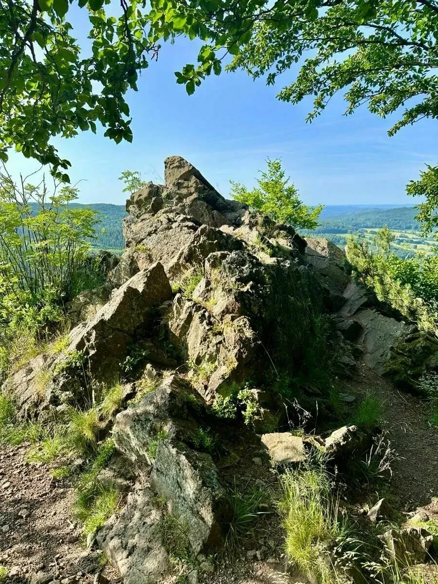 Ein felsiger Aussichtspunkt mit üppigem Grün und weitem Blick auf die Landschaft bei klarem Himmel.