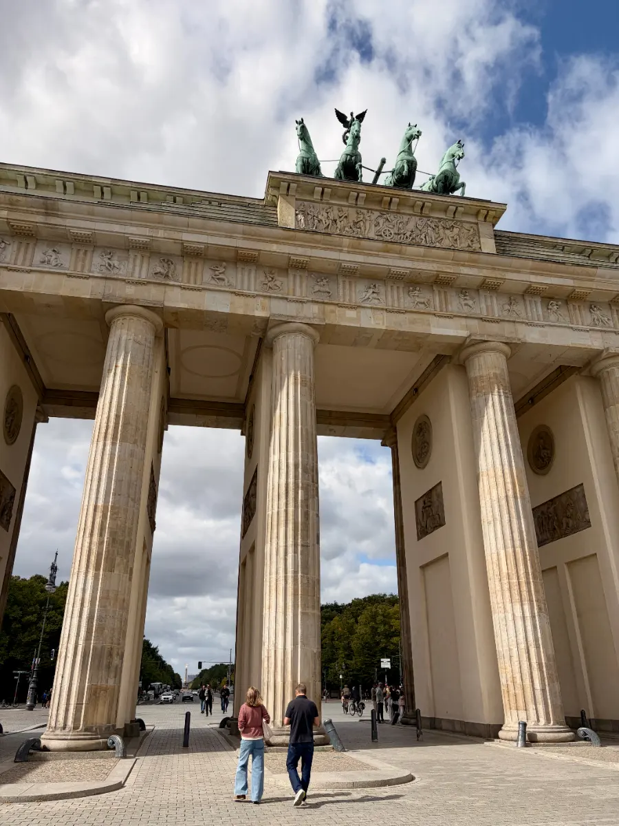 Brandenburger Tor in Berlin von unten fotografiert, mit Quadriga, hohen Säulen und Passanten unter bewölktem Himmel