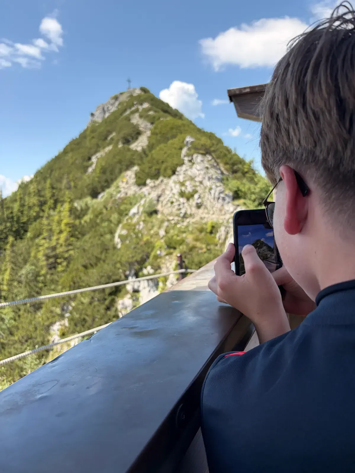 Ein Jugendlicher fotografiert von der Tegernseer Hütte aus den felsigen Roßstein vor blauem Himmel.