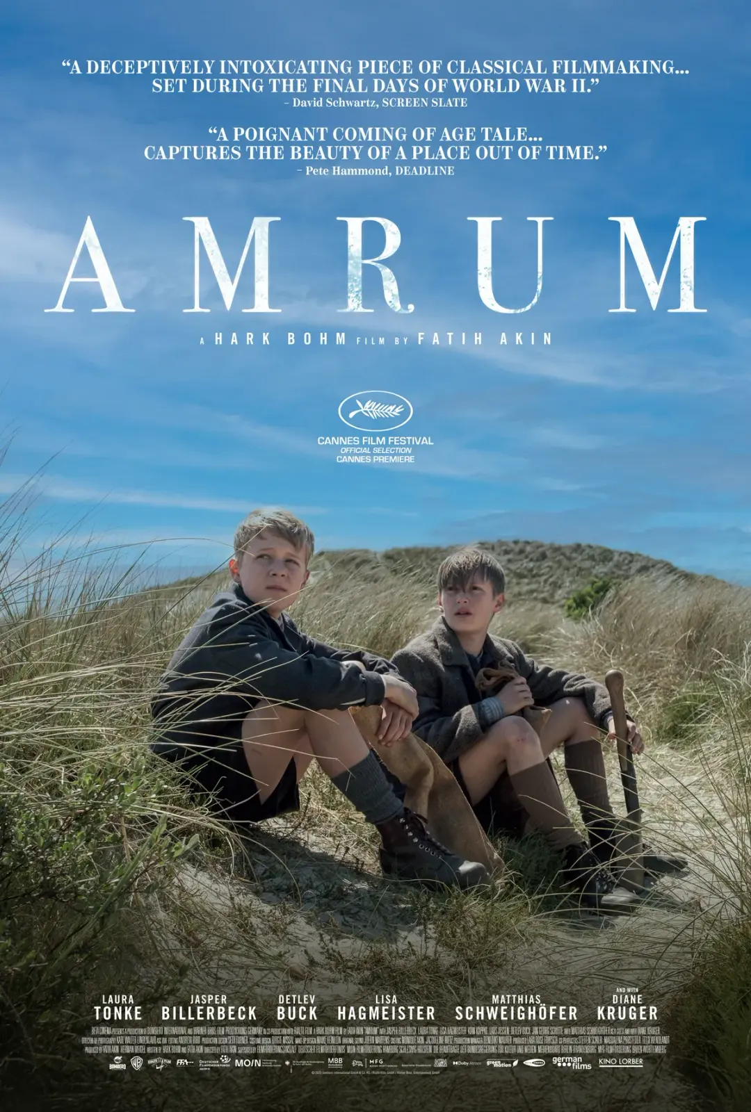 Zwei Jungen sitzen auf einem Hügel aus Sand und Gras, umgeben von Dünen. Der Filmname 