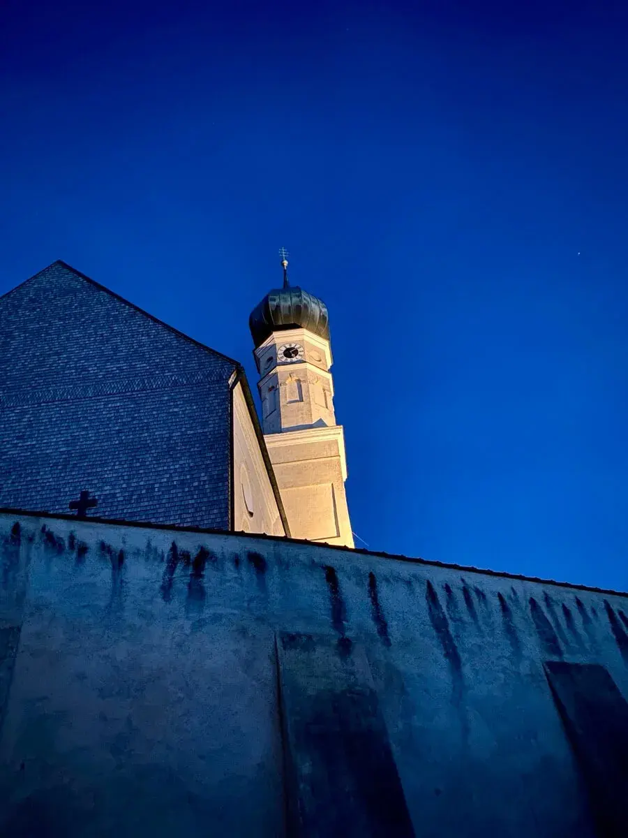 Die beleuchtete Kirche St. Georg in Finsing mit einem Turm und dunkelblauem Himmel im Hintergrund.