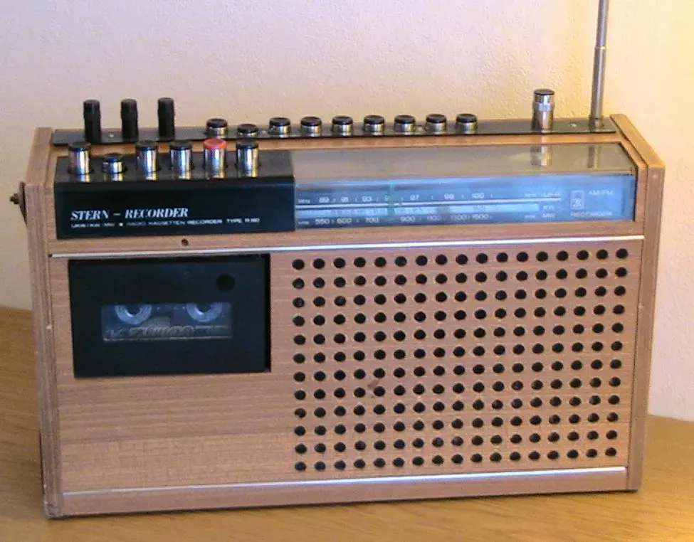 Der DDR Radio-Recorder Holzstern R160 aus Holz mit einer perforierten Front, einer Kassettenschublade auf der linken Seite und einem analogen Tuner-Bereich mit verschiedenen Reglern und Knöpfen an der Oberseite. Es gibt auch eine Antenne auf der rechten Seite.