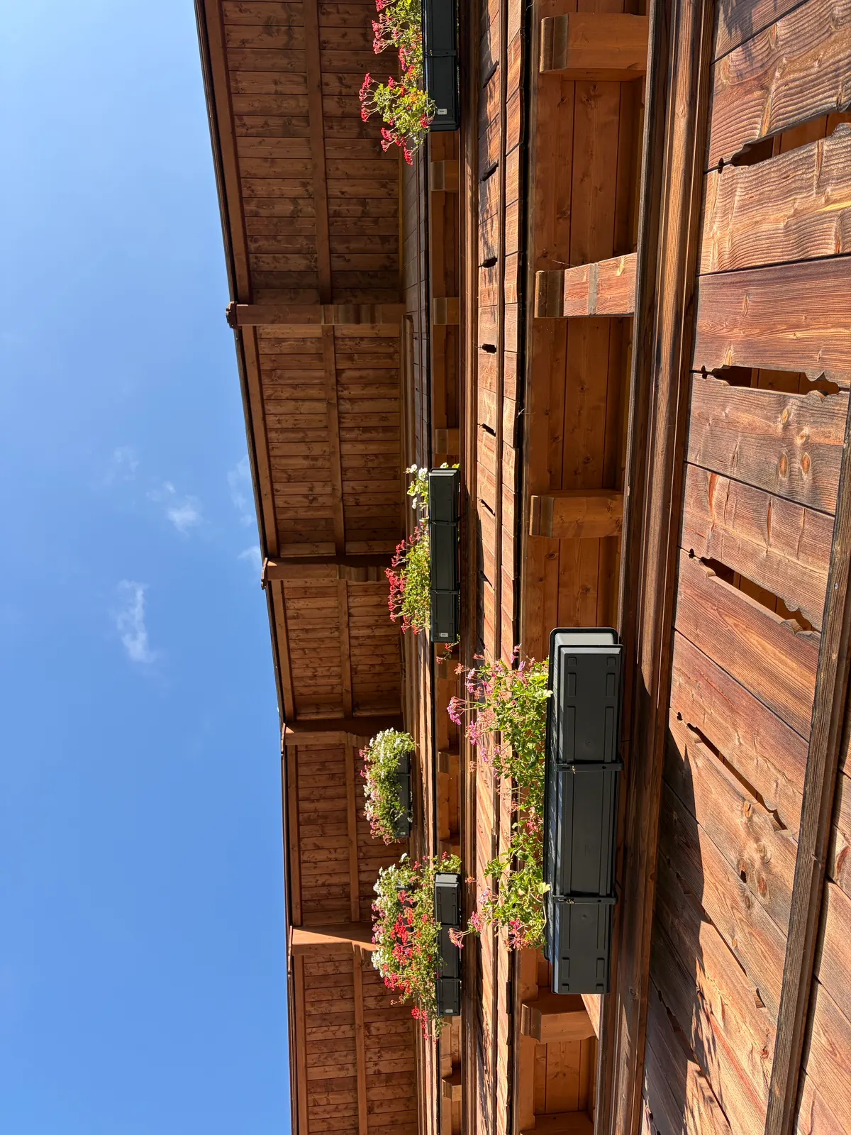 Alpine Holzfassade vom Gut Steinbach mit Blumenkästen und Balkonen vor blauem Himmel.