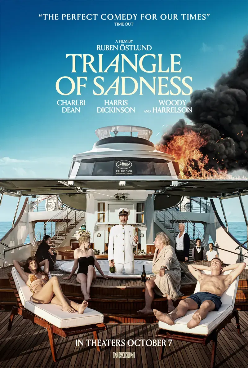 Poster for Triangle of Sadness showing wealthy passengers lounging on a yacht while a uniformed crew member stands center, with fire and black smoke rising behind the boat.