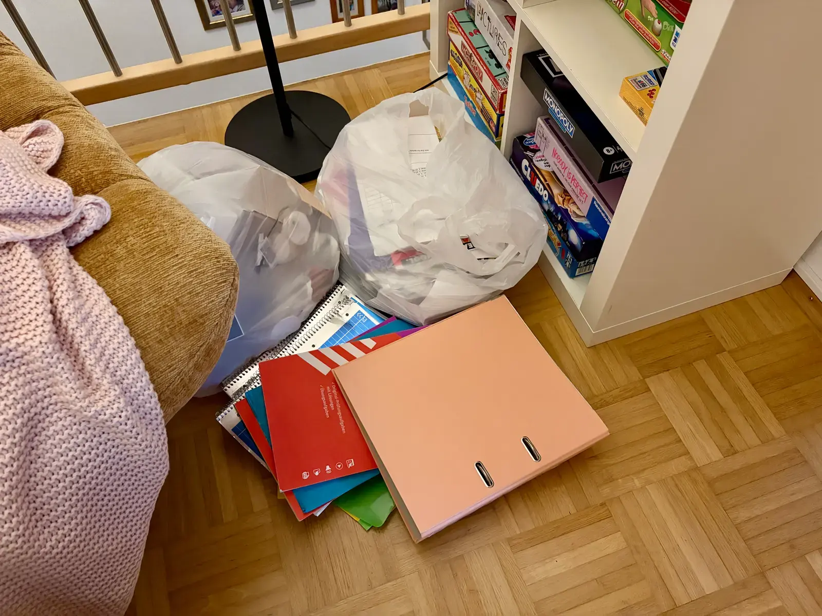 Vor einem Regal und einem Sofa liegen Müllsäcke, Schulhefte und ein rosa Ordner auf dem Parkettboden. Die Szene passt zum aufgeräumten Jugendzimmer, dessen Müll vor der Tür abgeladen wurde.