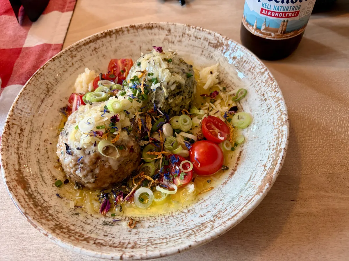 Teller mit zwei Knödeln in Buttersoße, garniert mit Frühlingszwiebeln, Kräutern und Kirschtomaten, daneben eine Bierflasche auf dem Tisch
