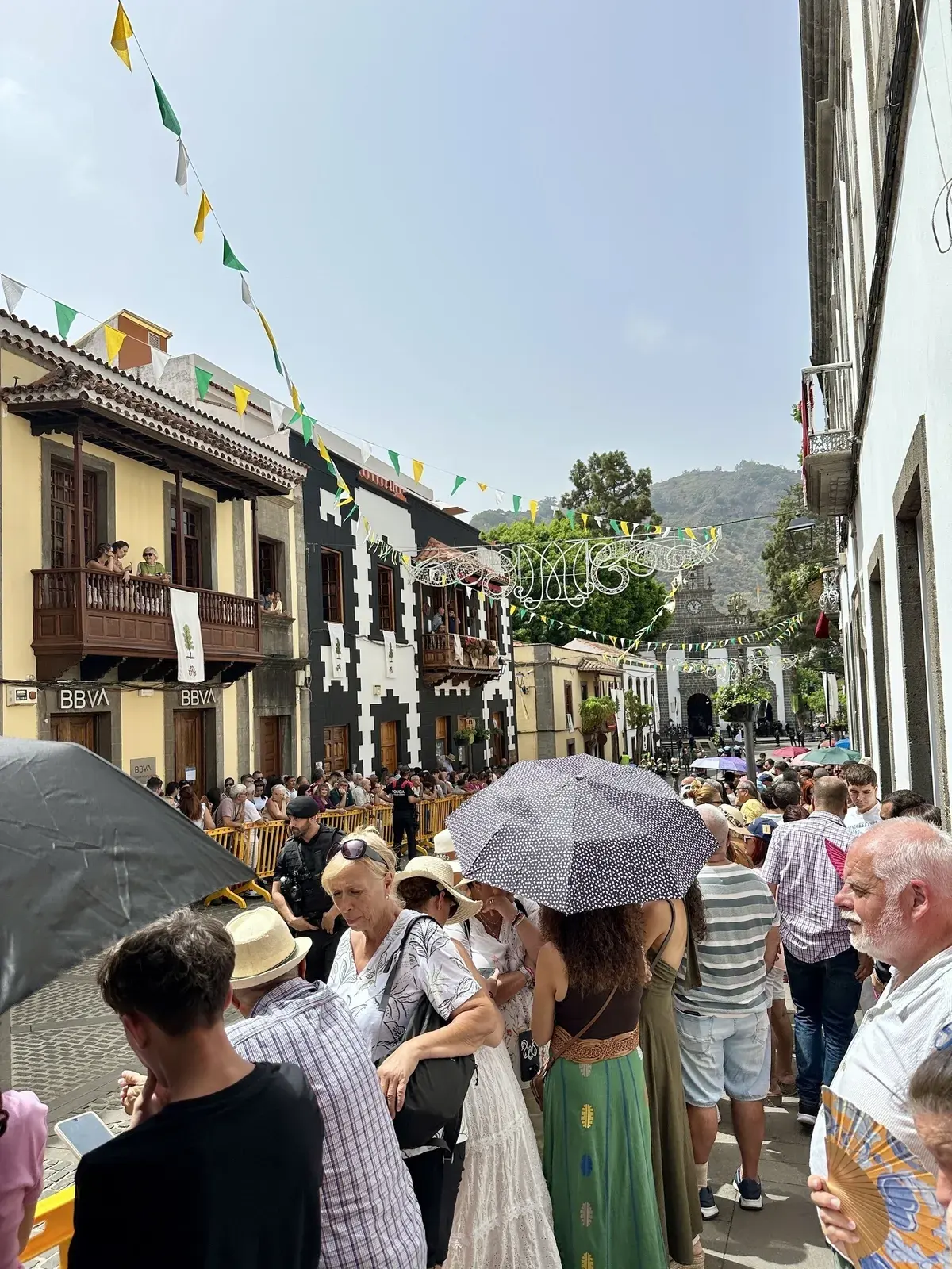 Eine Menschenmenge versammelt sich auf einer belebten Straße in einer spanischen Stadt, die mit bunten Wimpeln und typischen kanarischen Balkonen geschmückt ist.