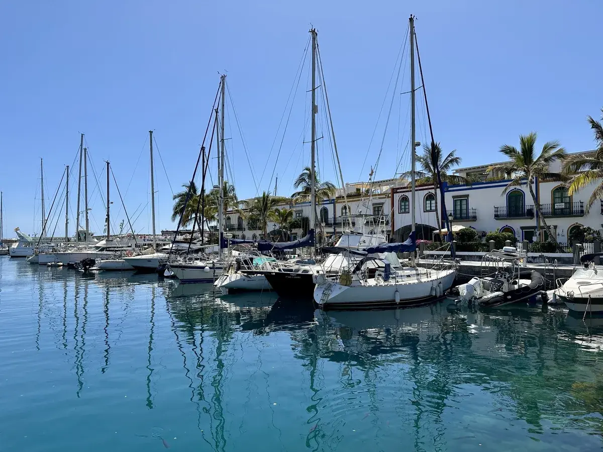Boote im Hafen von Puerto de Mogán vor hellen Gebäuden und Palmen.