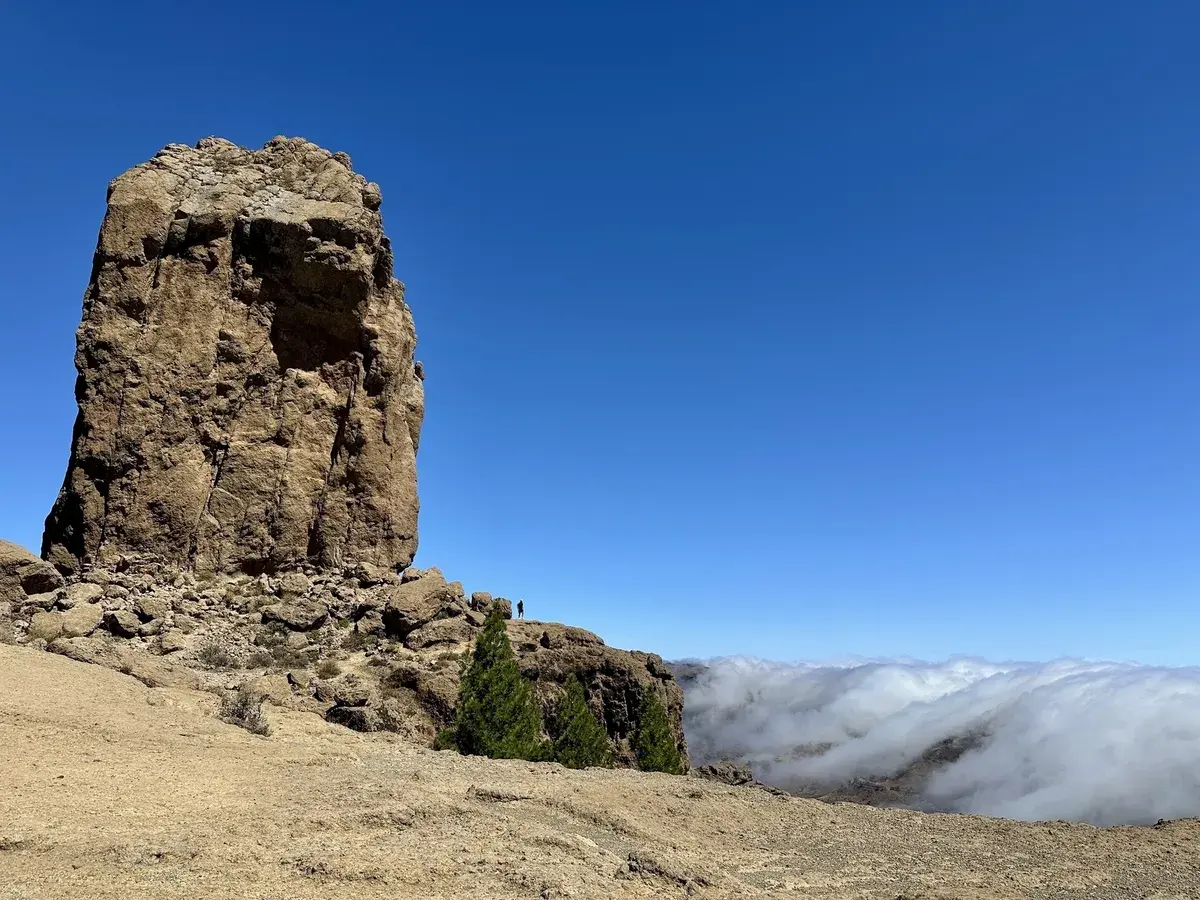 Der Roque Nublo, ein imposanter Felsmonolith und das Wahrzeichen von Gran Canaria erhebt sich über eine karge Landschaft, während sich am Horizont eine Wolkendecke erstreckt.