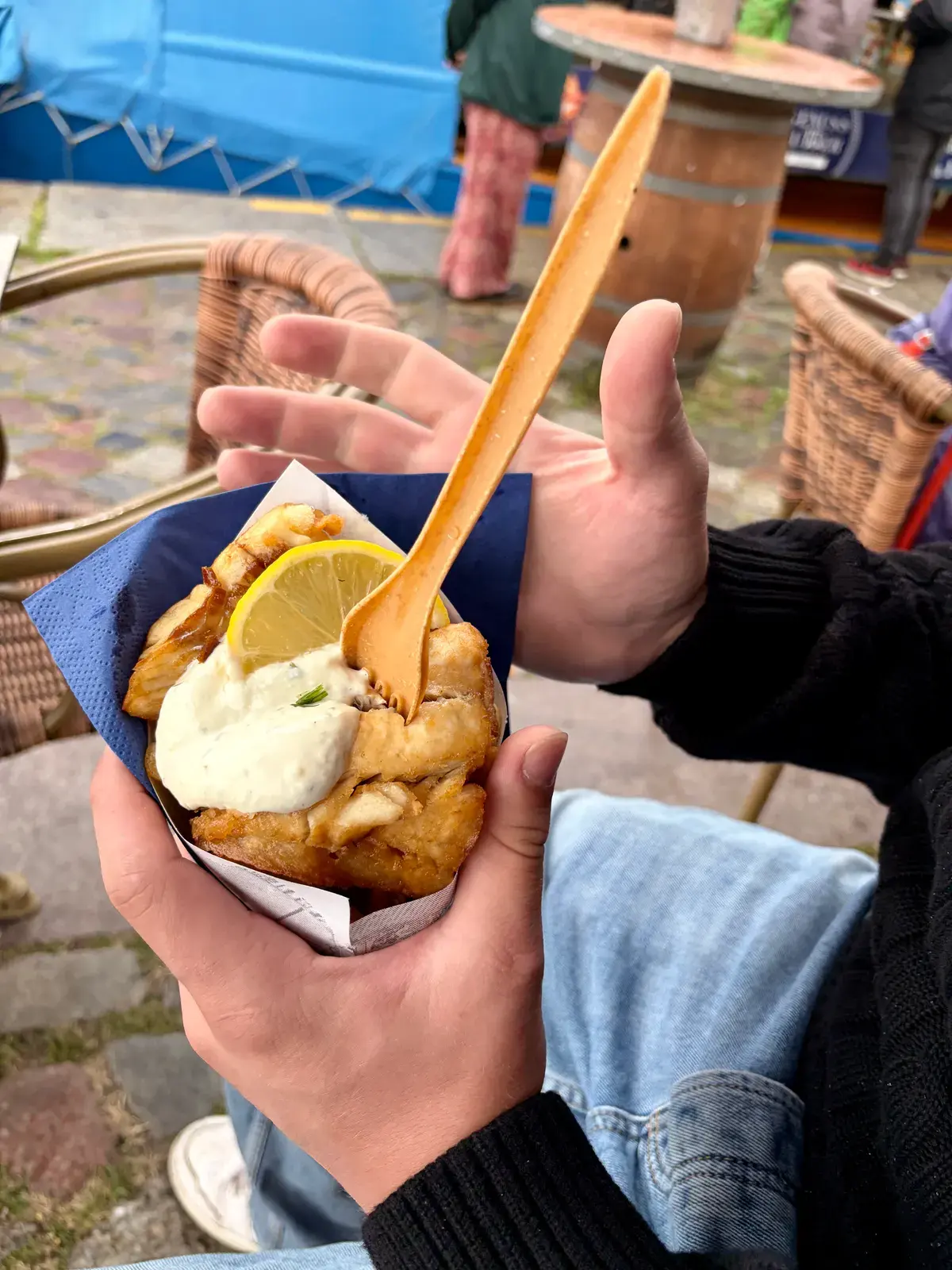 Fish and Chips mit Remoulade und Zitronenscheibe in den Händen, draußen an einem regennassen Tisch im Hafen von Stralsund.