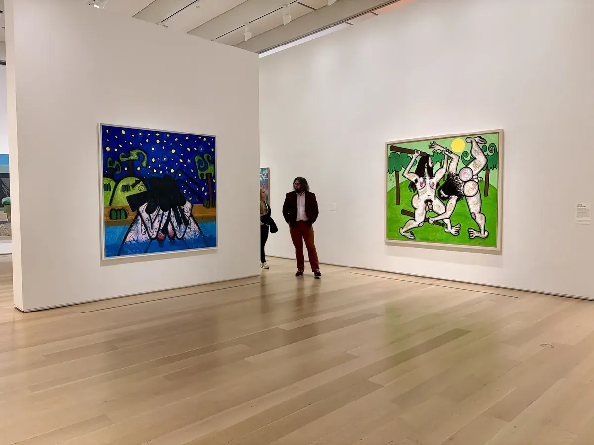Zwei lebendige, abstrahierte Kunstwerke hängen an den Wänden eines modernen Ausstellungsraums. Im Vordergrund stehen zwei Besucher, die die Kunstwerke betrachten.