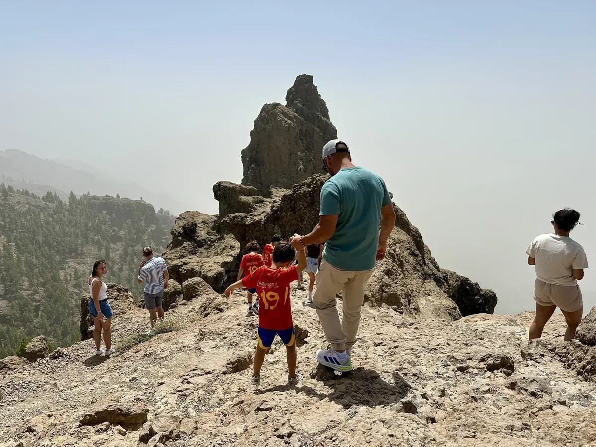 Eine Gruppe von Menschen steht auf felsigem Gelände am Pico de las Nieves auf Gran Canaria mit Bergen im Hintergrund.