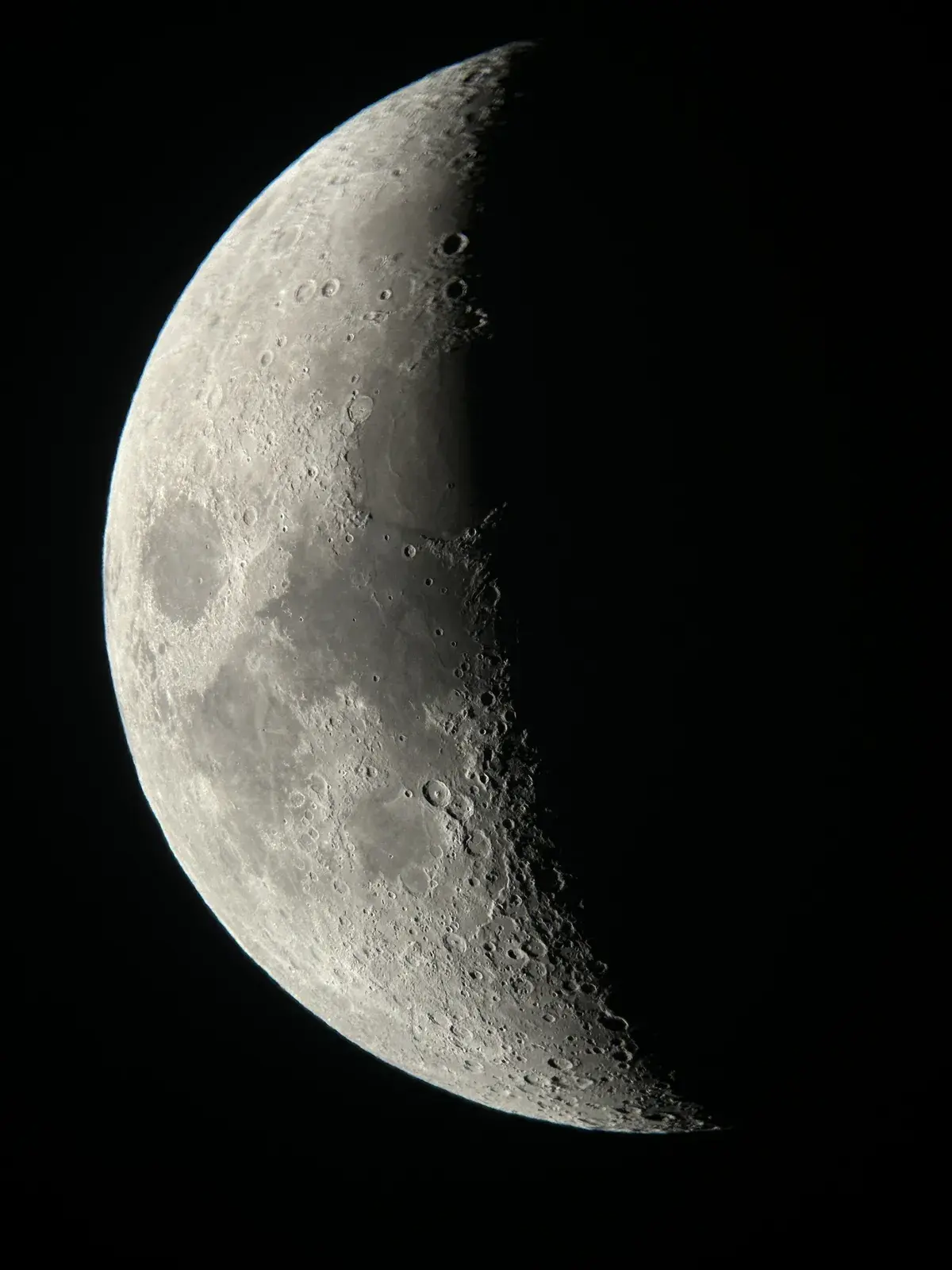 Ein zunehmender Halbmond mit deutlich sichtbaren Kratern leuchtet vor einem dunklen Hintergrund.