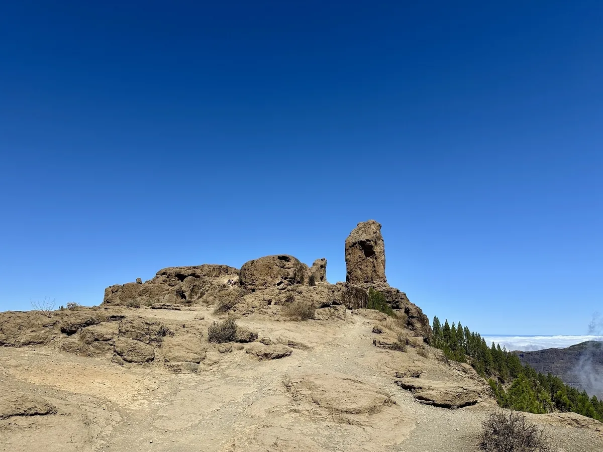 Ein Felsplateau mit dem markanten Roque Nublo unter klarem, blauem Himmel in der bergigen Landschaft von Gran Canaria.