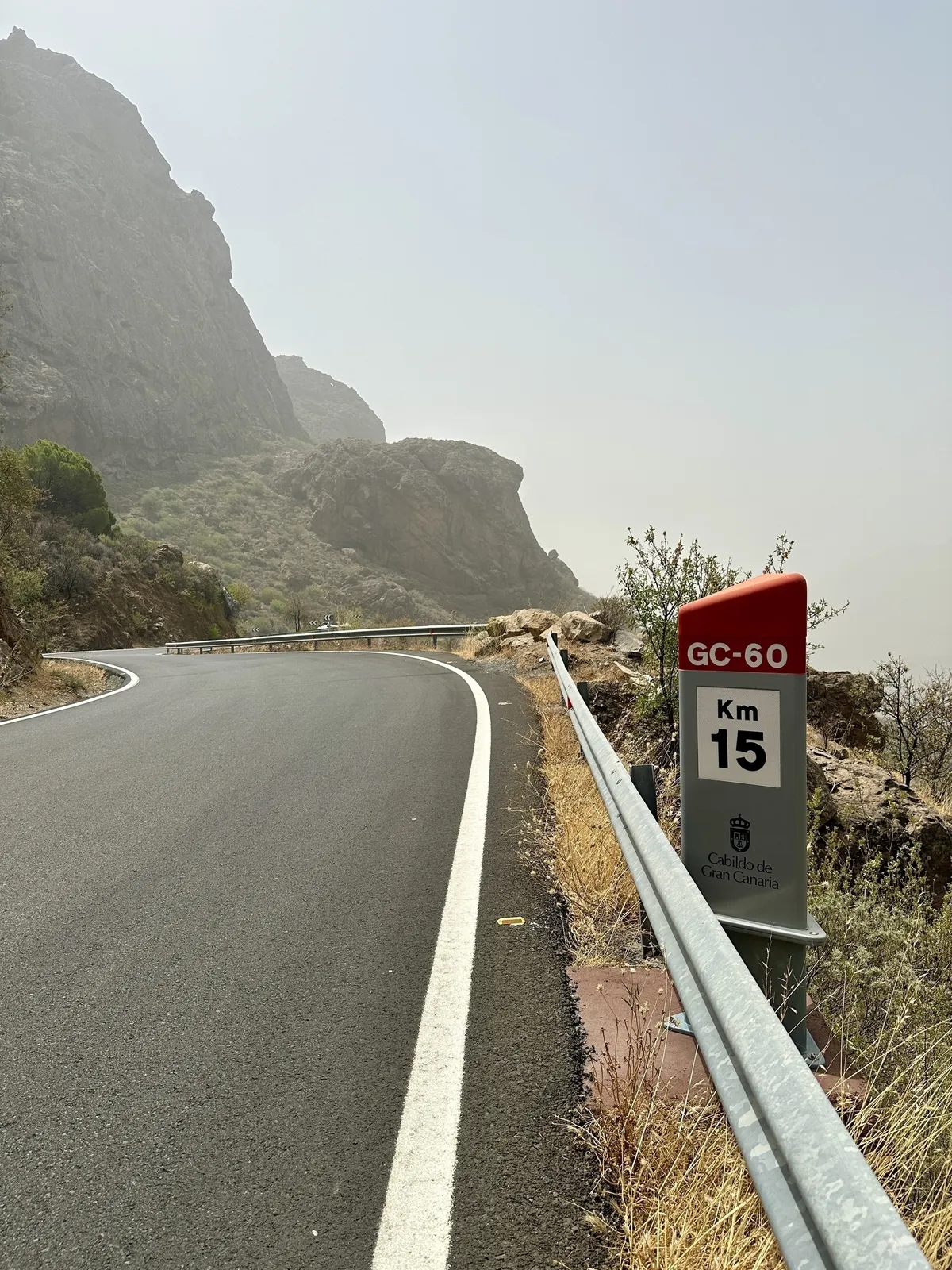 Eine kurvenreiche Bergstraße in Gran Canaria führt an einem Kilometerstein vorbei, umgeben von karger Landschaft und Felsen.