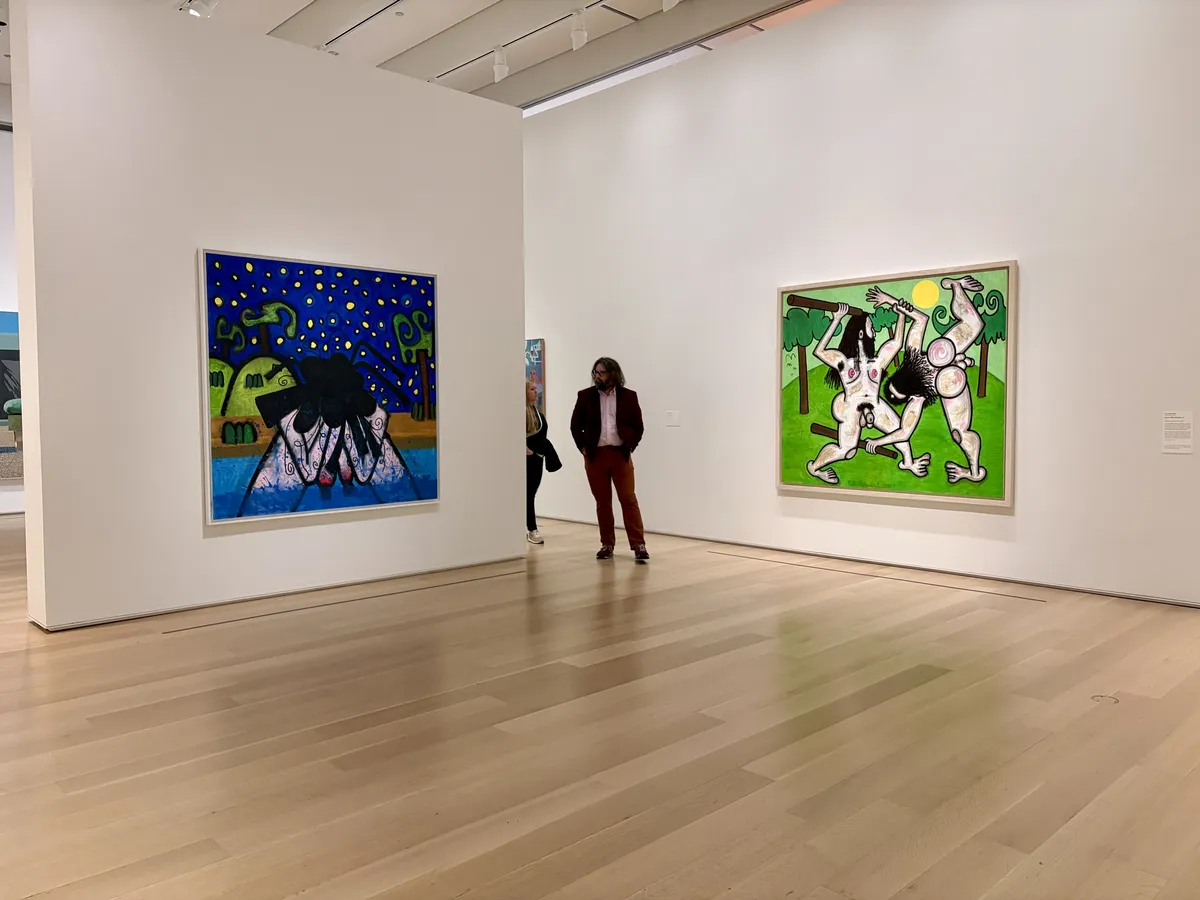Zwei lebendige, abstrahierte Kunstwerke hängen an den Wänden eines modernen Ausstellungsraums. Im Vordergrund stehen zwei Besucher, die die Kunstwerke betrachten.
