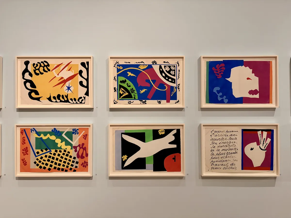 Sechs gerahmte Kunstwerke hängen an einer hellen Wand. Die Bilder zeigen eine Mischung aus abstrakten Formen und lebhaften Farben, darunter geometrische und organische Motive sowie Text.