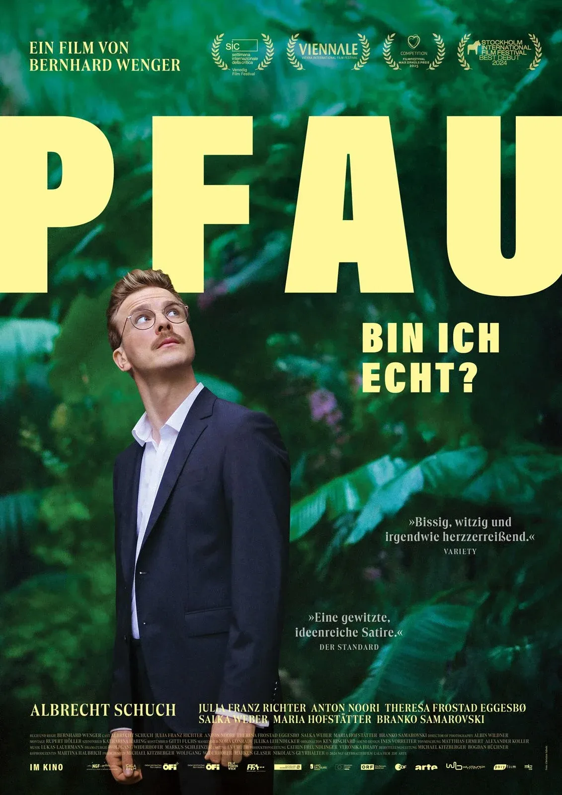 Eine Person in Anzug steht inmitten von grüner Vegetation und schaut nachdenklich in die Ferne. Der Titel des Films 
