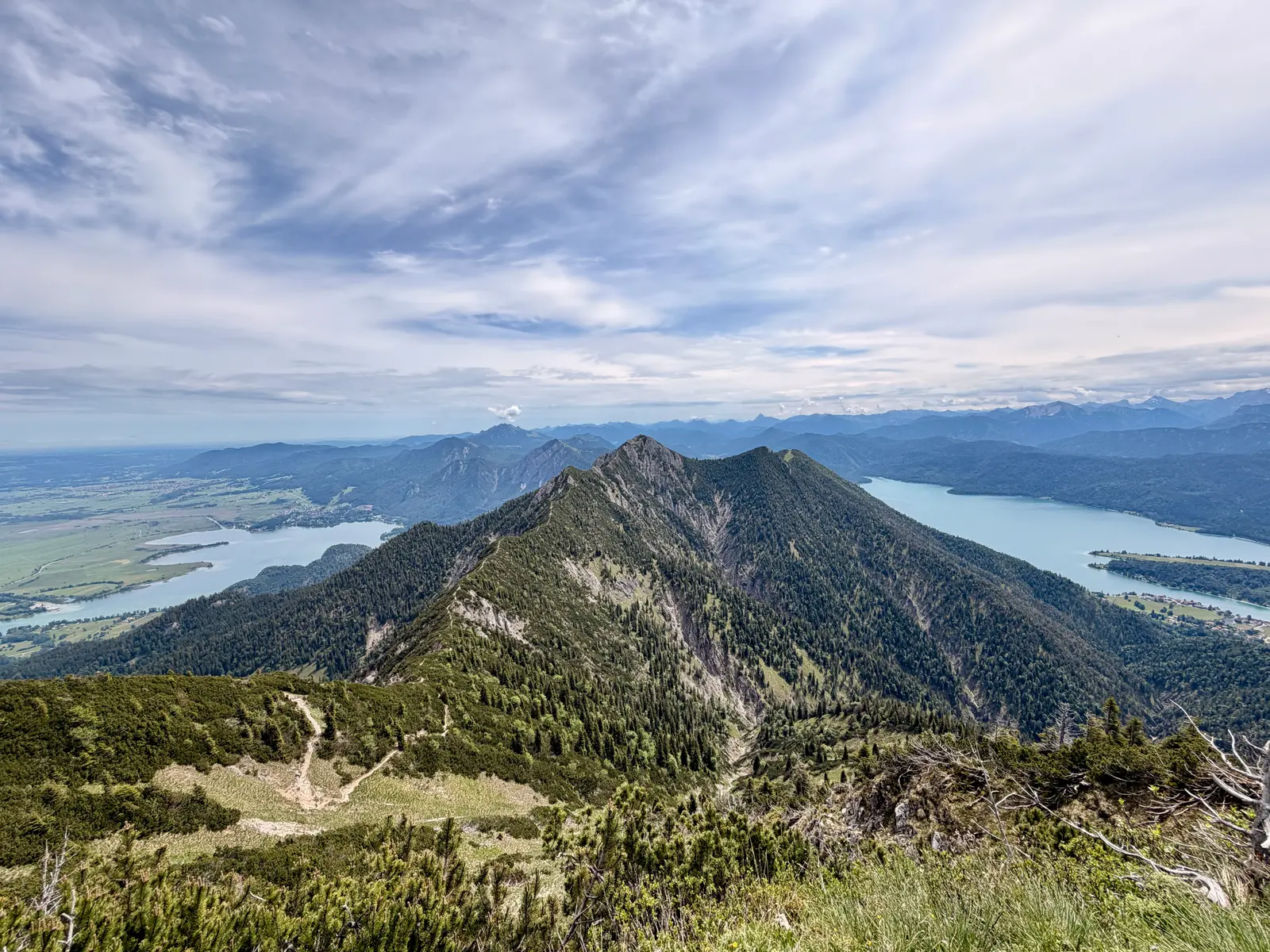 Blick vom Heimgarten auf den Herzogstand. Links der Kochlsee und rechts der Walchsensee unter einem sonnigen Himmel.