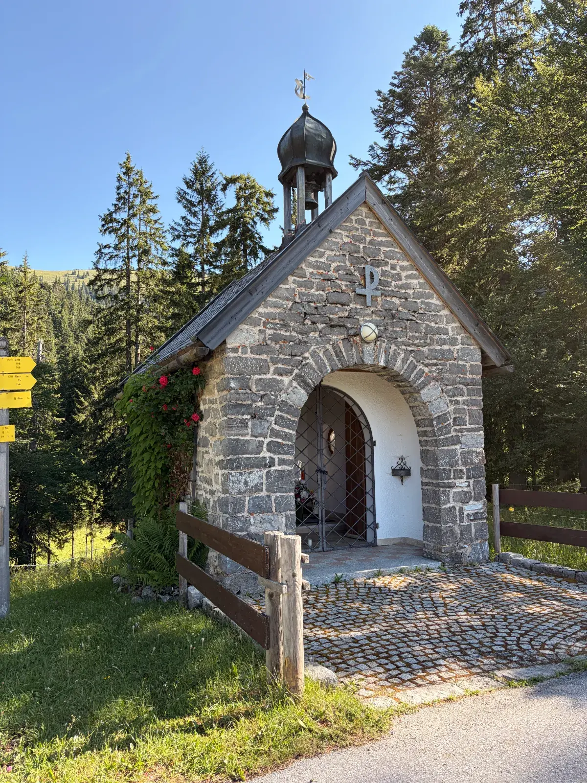 Steinerne St.-Michaels-Kapelle an der Schwarzenkopfhütte bei Spitzingsee, umgeben von Bäumen und in der Morgensonne.