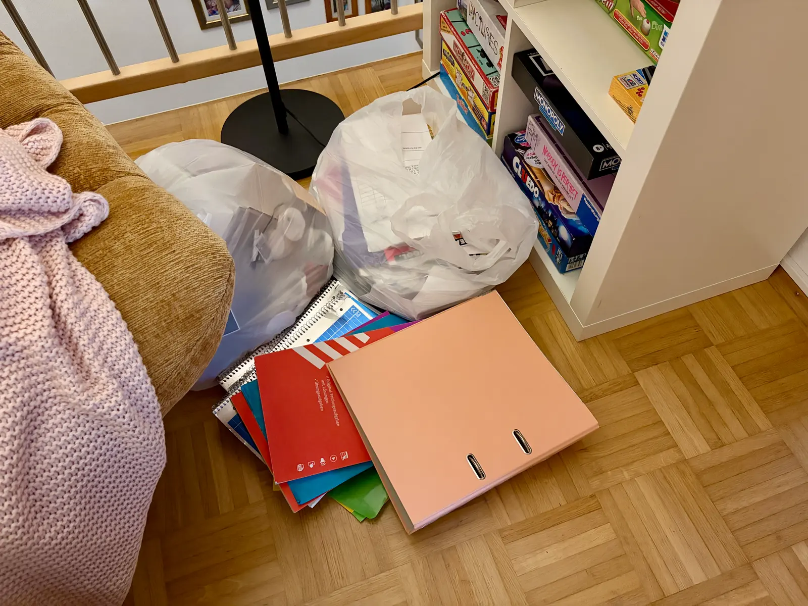 Vor einem Regal und einem Sofa liegen Müllsäcke, Schulhefte und ein rosa Ordner auf dem Parkettboden. Die Szene passt zum aufgeräumten Jugendzimmer, dessen Müll vor der Tür abgeladen wurde.