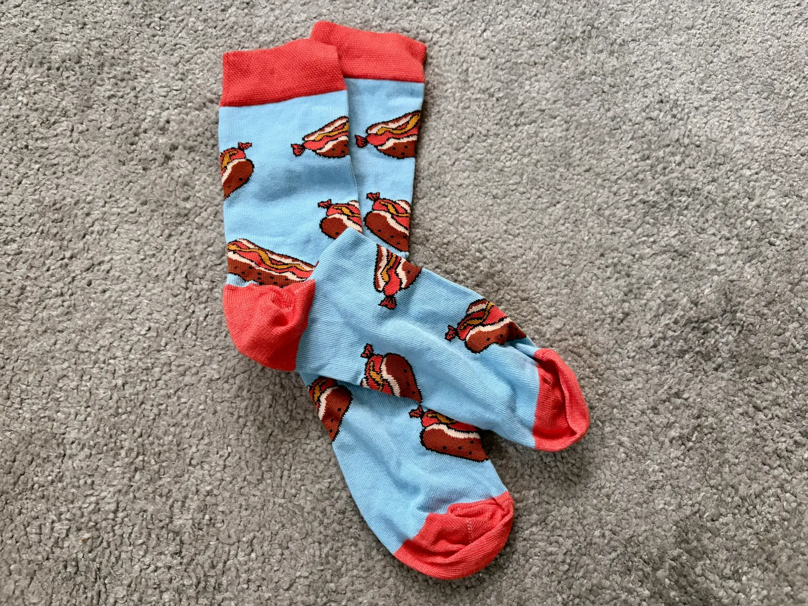 Ein paar blau-orange-farbige Socken mit einem Bratwurstmuster liegen auf einem grauen Teppich